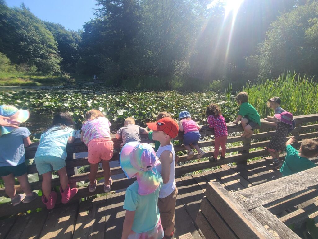 Children at Roots & Rhythms Summer Camp climb fences to investigate the water in McLane Creek